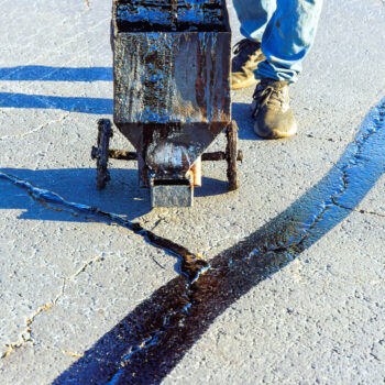 An asphalt patcher performs coated filling asphalt cracks sealing bitumen emulsion road surface restoration