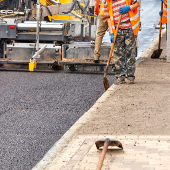 An industrial worker laying a layer of new hot asphalt on the carriageway